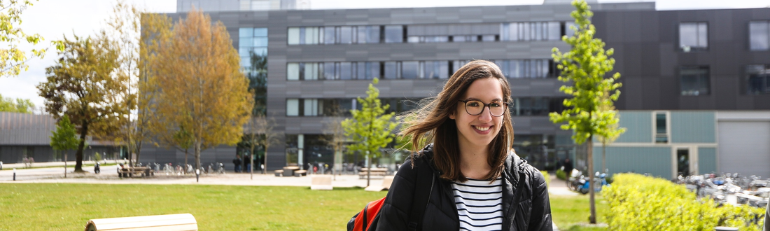 Studentin vor Campuswiese, Gebäude G im Hintergrund