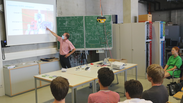 Professor zeigt auf die Bildschirmpräsentation im Hörsaal vor den Schülern