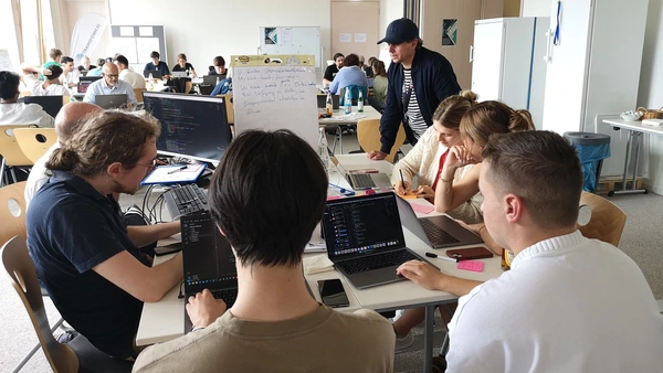 A room full of people sitting in groups at tables and working on their laptops.