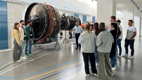 A group of young people and an MTU employee look at a turbine.