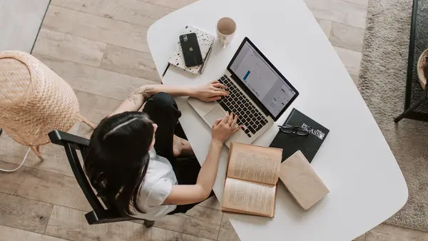  A female student sits at a table with laptop and books