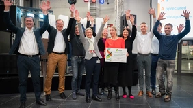 Ten cheering people, a woman in the middle holds up a certificate.