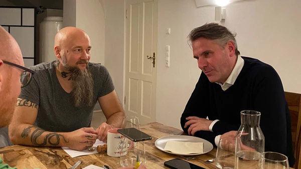 Three men are sitting at a set table and talking.