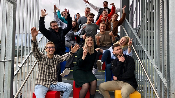 Prof. Huber and students sitting an stairs outside raising their hands.