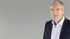 Prof. Dr. Marc Knoppe in a dark suit in front of a gray background