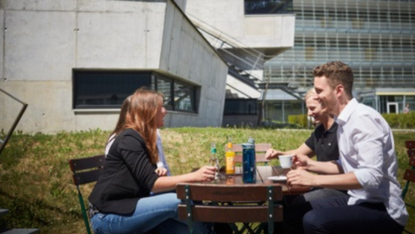 Menschen sitzen auf Bank auf Campus Wiese